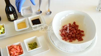 Hands of professional chef adding ingredients to red or diced tuna fish