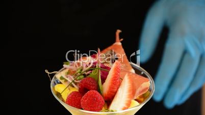Hands of professional chef decorating cup mango fruit and ham with herbs detail