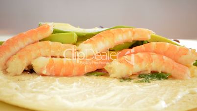 Professional chef hands rolling a wheat cake with prawns, avocado and herbs