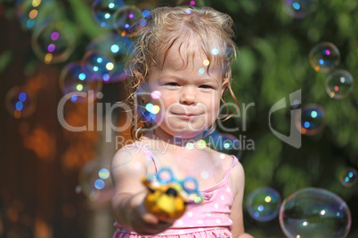 Happy little girl playing with soap bubbles in the garden