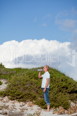 young man ist drinking water summertime dune beach sky