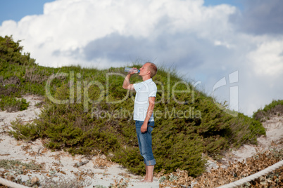 young man ist drinking water summertime dune beach sky