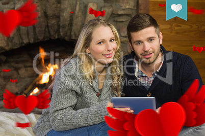 Composite image of couple using tablet pc in front of lit firepl