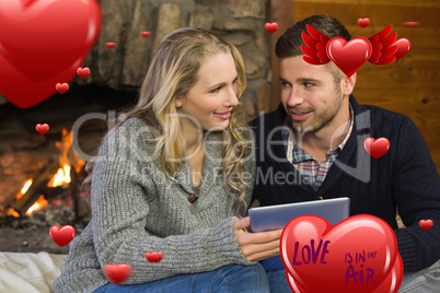 Composite image of couple using tablet pc in front of lit firepl
