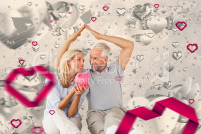 Composite image of happy couple sitting and sheltering piggy ban