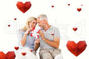 Composite image of happy couple sitting and holding present