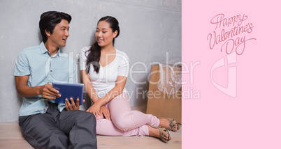 Composite image of happy couple sitting on floor using tablet su