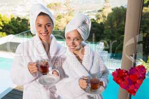 Composite image of smiling women in bathrobes having tea
