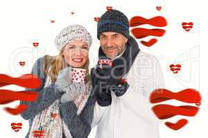 Composite image of happy couple in winter fashion holding mugs