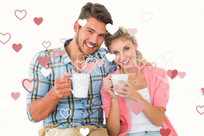 Composite image of attractive young couple sitting holding mugs