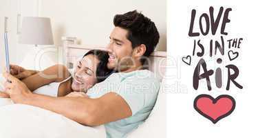 Composite image of attractive couple lying in bed with tablet pc