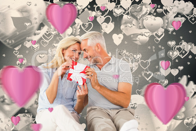 Composite image of happy couple sitting and holding present