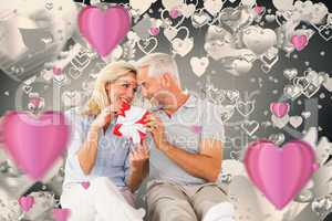 Composite image of happy couple sitting and holding present