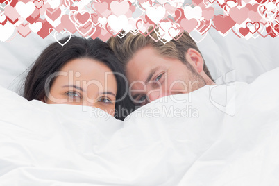 Composite image of couple hiding under the duvet