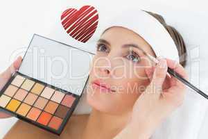 Composite image of hand applying eyeshadow to beautiful woman