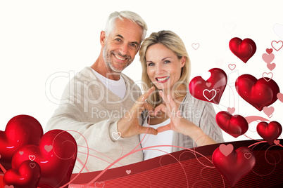 Composite image of happy couple forming heart shape with hands