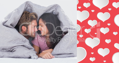 Composite image of attractive couple wrapped in the duvet