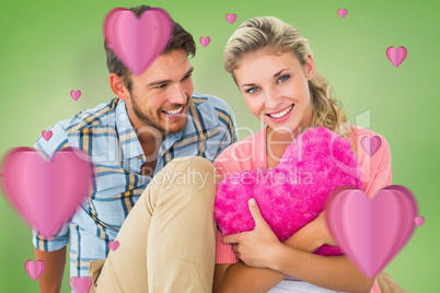 Composite image of attractive young couple sitting holding heart Composite image of attractive young couple sitting holding heart