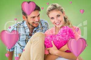 Composite image of attractive young couple sitting holding heart