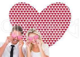 Composite image of attractive young couple holding pink hearts o