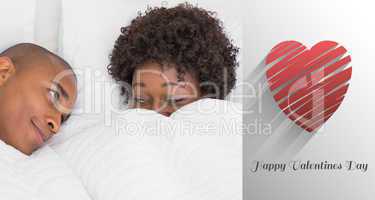 Composite image of happy couple lying in bed under the duvet