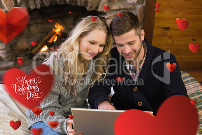 Composite image of couple using laptop in front of lit fireplace