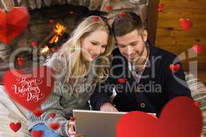 Composite image of couple using laptop in front of lit fireplace