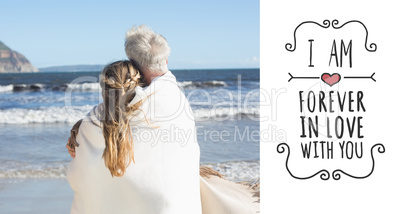 Composite image of couple wrapped up in blanket on the beach loo