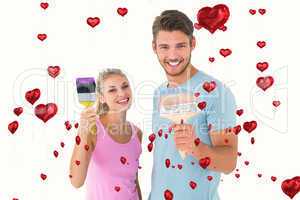 Composite image of young couple smiling and holding paintbrushes