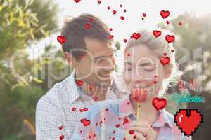 Composite image of young couple holding a flower in park