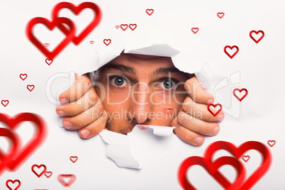 Composite image of young man looking through paper rip