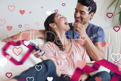 Composite image of playful couple watching tv while eating popco