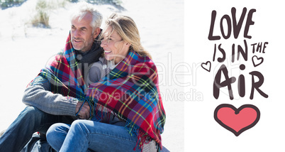 Composite image of happy couple wrapped up in blanket sitting on