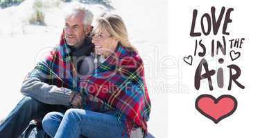 Composite image of happy couple wrapped up in blanket sitting on