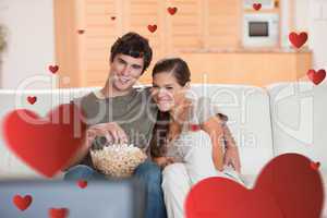 Composite image of couple with popcorn on the sofa watching a mo