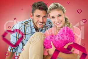 Composite image of attractive young couple sitting holding heart