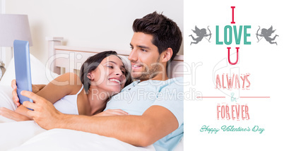 Composite image of attractive couple lying in bed with tablet pc