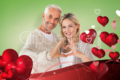 Composite image of happy couple forming heart shape with hands