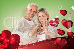 Composite image of happy couple forming heart shape with hands