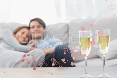 Composite image of couple resting on a couch with flutes of cham