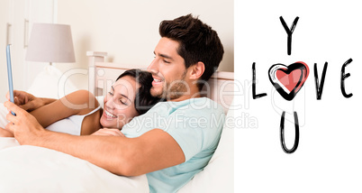 Composite image of attractive couple lying in bed with tablet pc