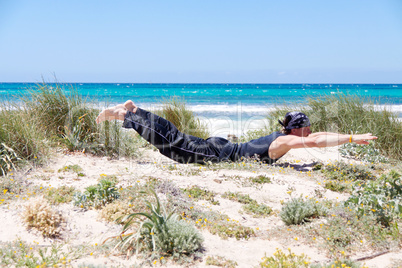 man doing pilates exercises on beach in summer