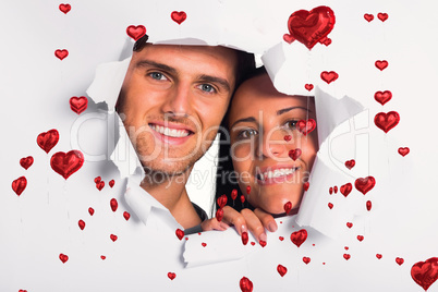 Composite image of young couple looking through paper rip