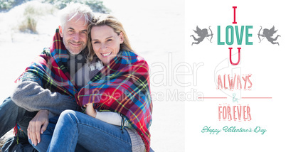 Composite image of happy couple wrapped up in blanket sitting on