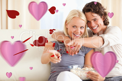 Composite image of cute couple watching tv while eating popcorn