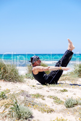 man doing pilates exercises on beach in summer