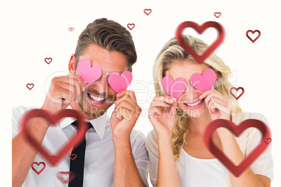 Composite image of attractive young couple holding pink hearts o