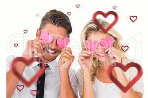 Composite image of attractive young couple holding pink hearts o