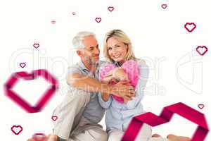 Composite image of happy couple sitting and holding heart pillow