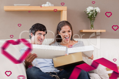 Composite image of couple on the couch opening parcel